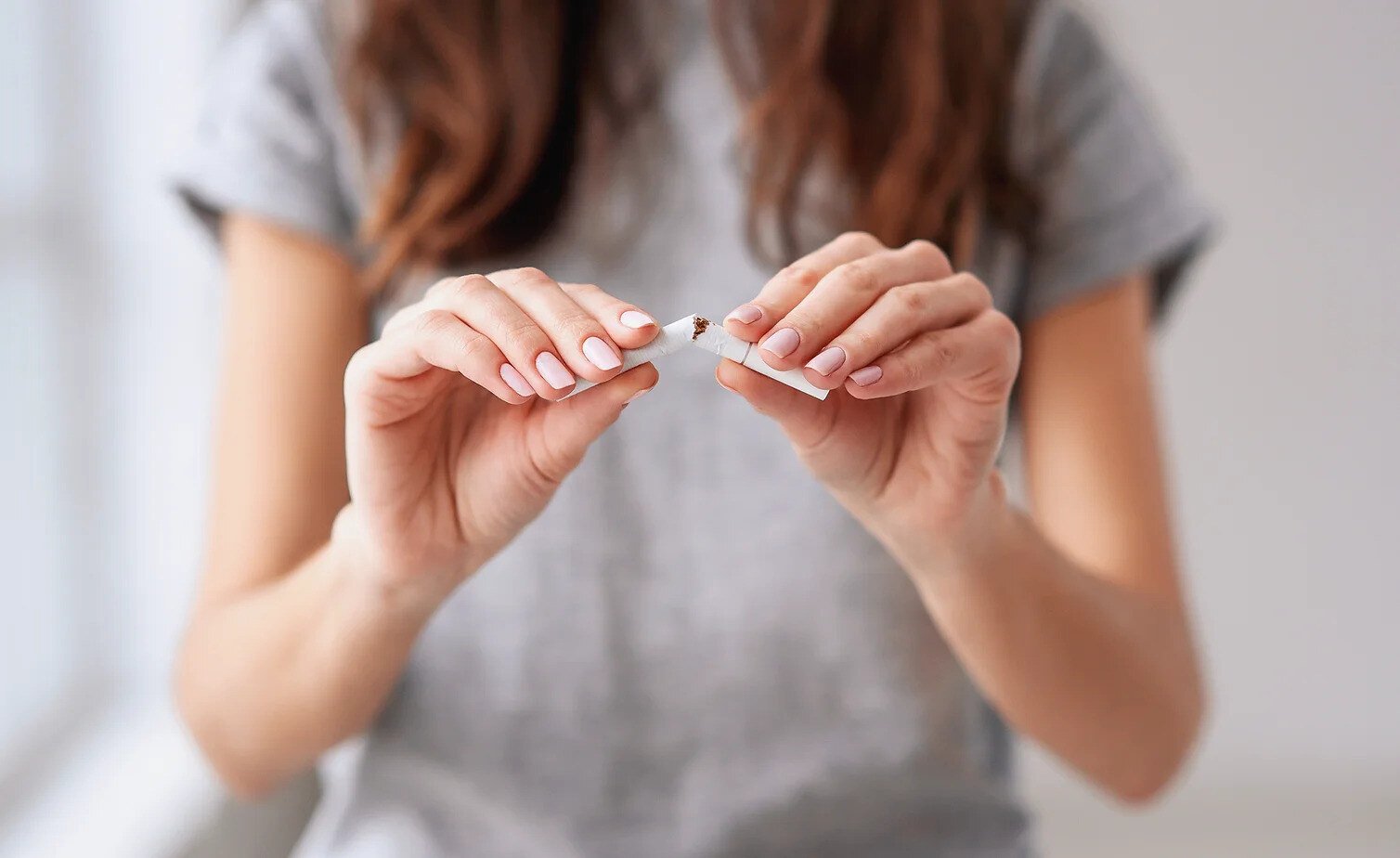 Stop smoking cigarettes concept. Portrait of beautiful smiling girl holding broken cigarette in hands.