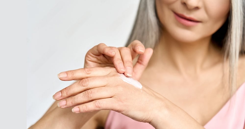Mature beautiful senior mid age older Asian woman of 50s years applying putting skin care lotion hand cream doing her everyday routine.